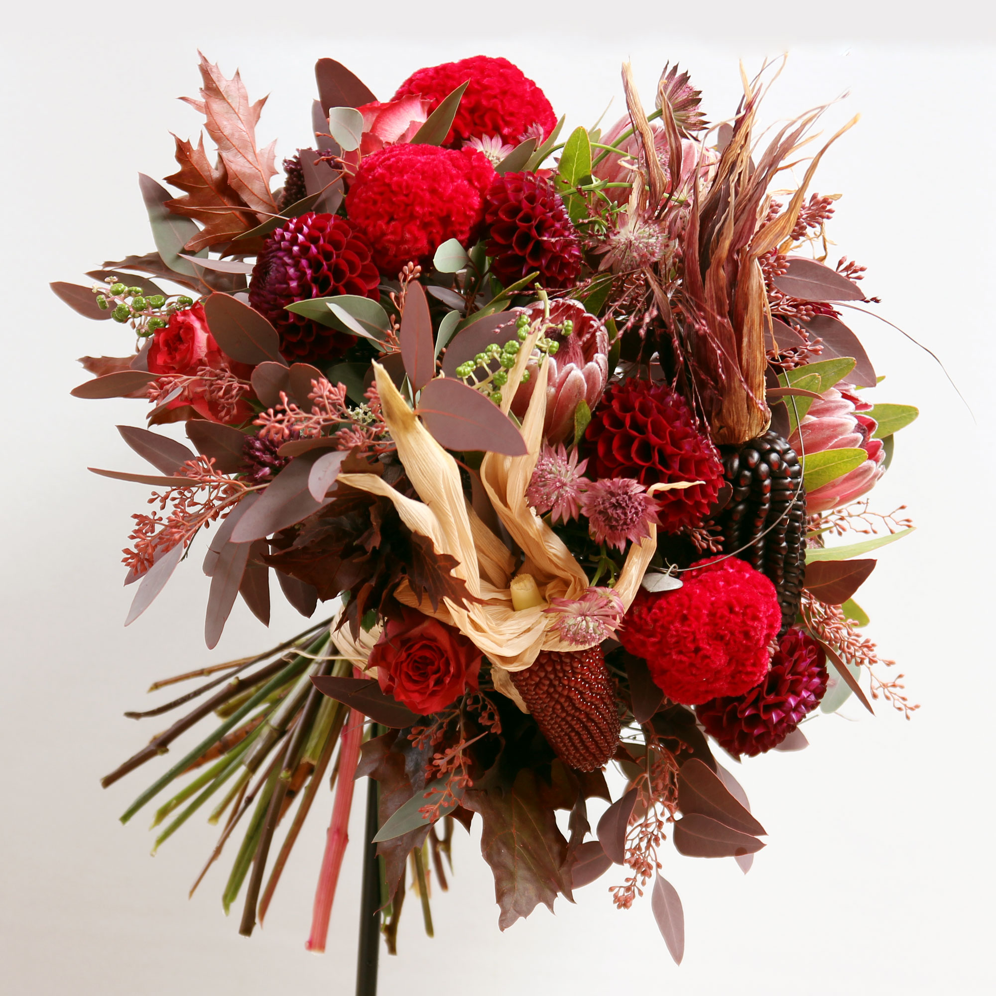 Bouquet composé de dalhias, de célosies crête de coq, de banksias, d’astrancias, d’eucalyptus, de roses et d’épis de maïs.